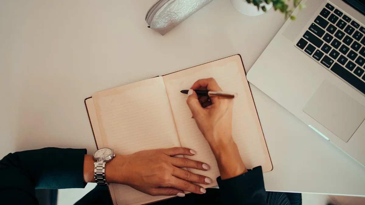 Student drafting a motivation letter for Turkish universities in a notebook next to a laptop